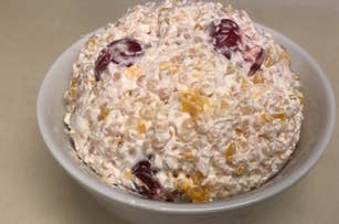 A bowl of fruit salad with whipped topping, featuring visible grapes and pineapple chunks