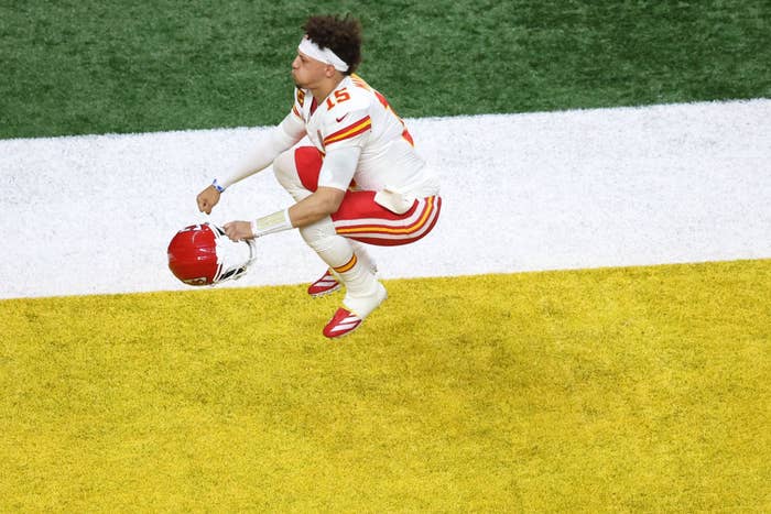 Football player in uniform performs a high jump, holding helmet, on a field