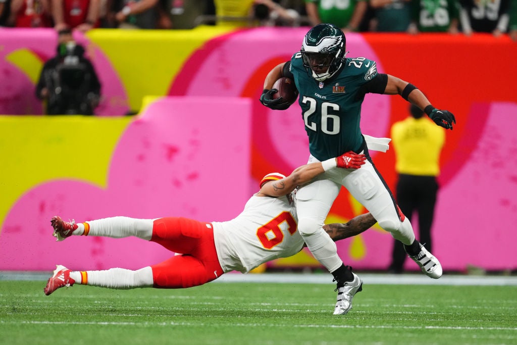 Football player in uniform evades tackle, holding ball tightly. Dynamic action scene on colorful field backdrop