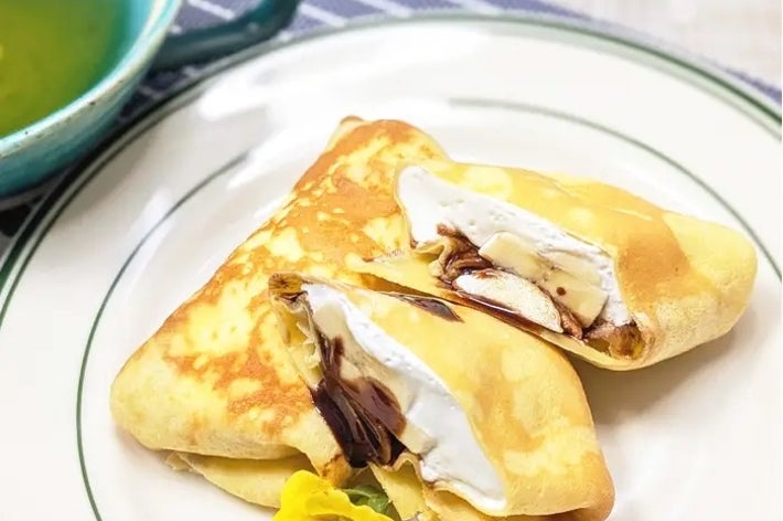 皿に乗ったクリームとチョコレート入りのクレープ。花の飾り付き。隣に緑の飲み物。