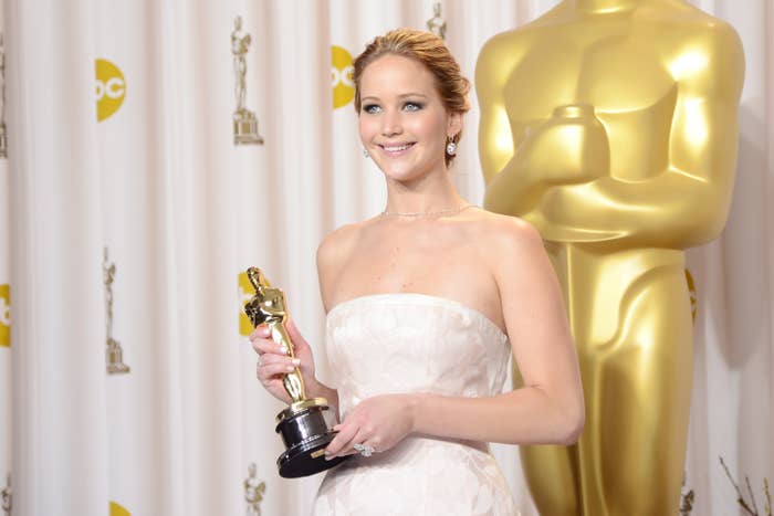 Actress in elegant strapless gown holds an Oscar statue, smiling at an awards event