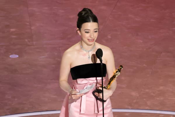 Person in elegant gown holding a trophy, speaking at a podium on stage