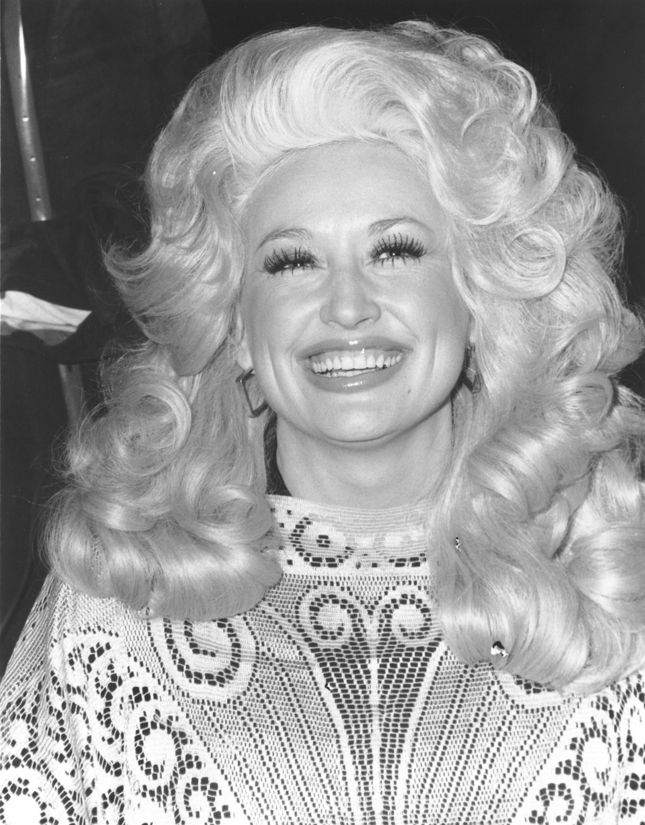 Person with voluminous, curly hairstyle smiling, wearing intricate patterned top