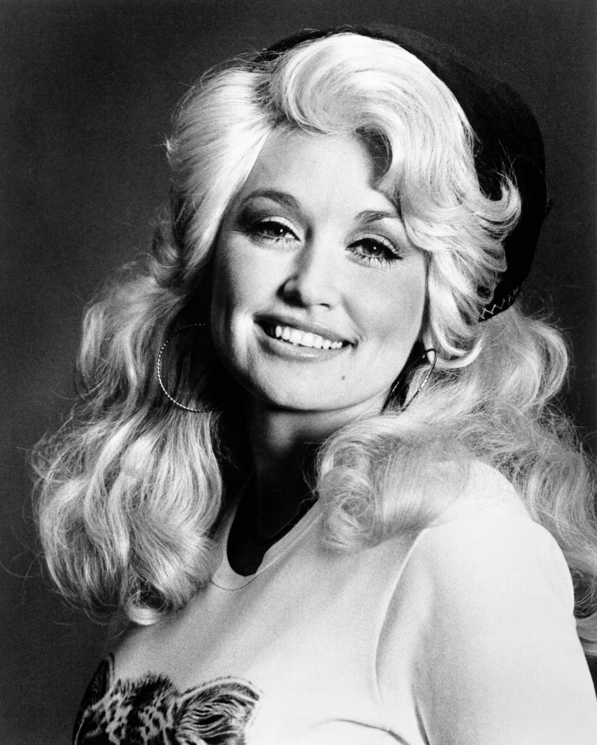 Person with voluminous hair, wearing a beret, hoop earrings, and a top with a graphic design. Smiling at the camera