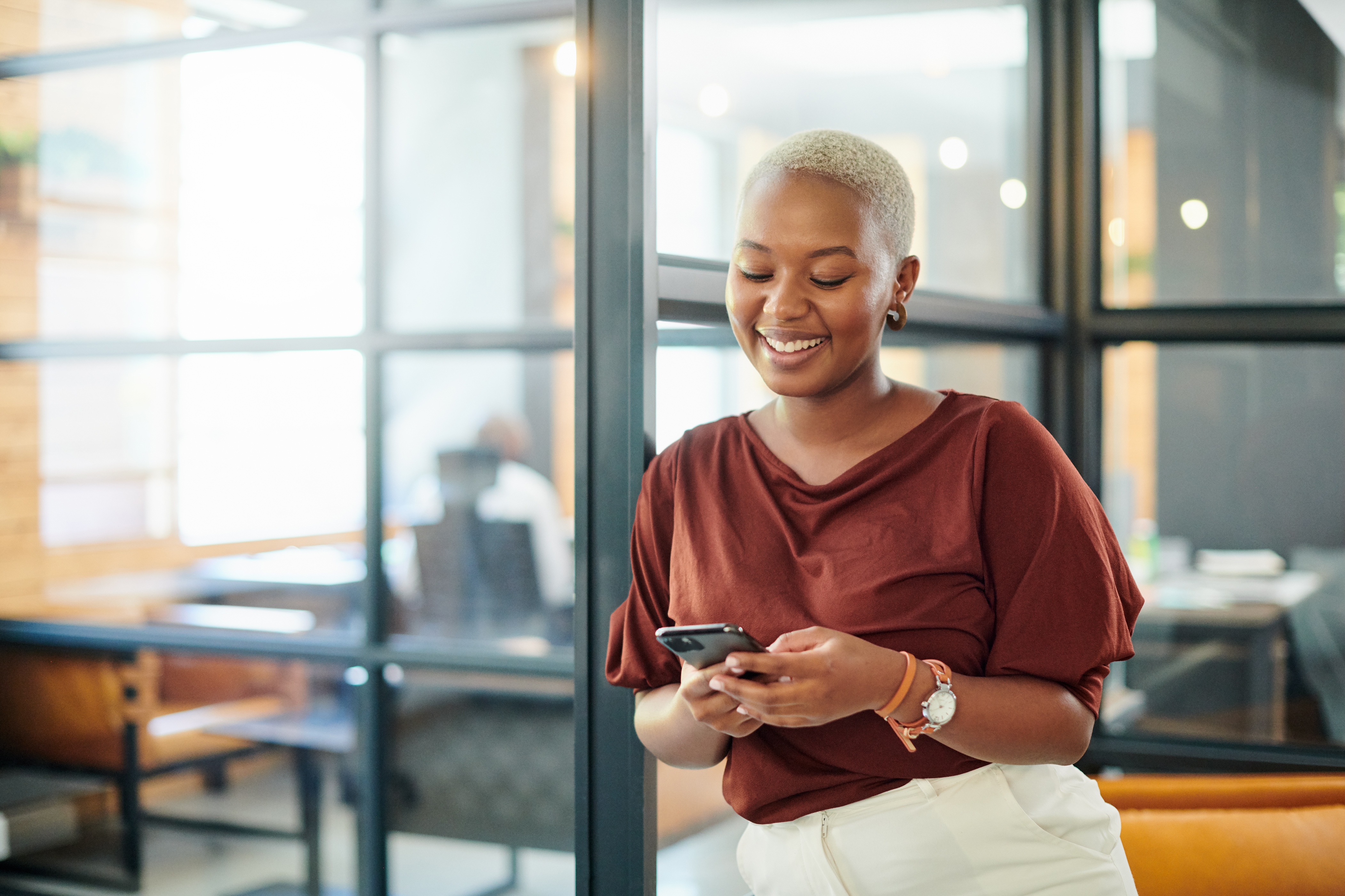Person smiler mens du bruker en smarttelefon i moderne kontorinnstillinger