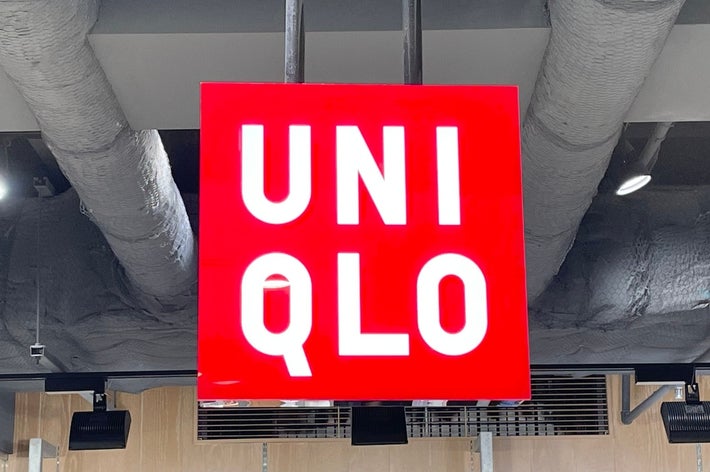 Store sign reads &ldquo;UNIQLO&rdquo; hanging from the ceiling above shelves of folded clothing