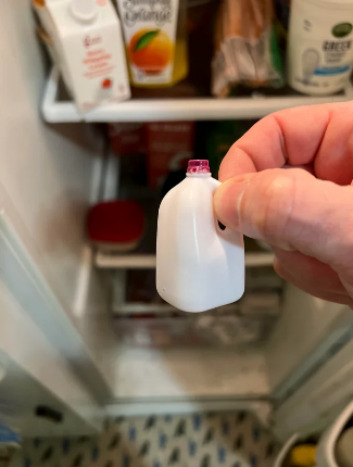 Person holding a miniature jug of beverage  successful  beforehand   of an unfastened  fridge with assorted  containers disposable   inside