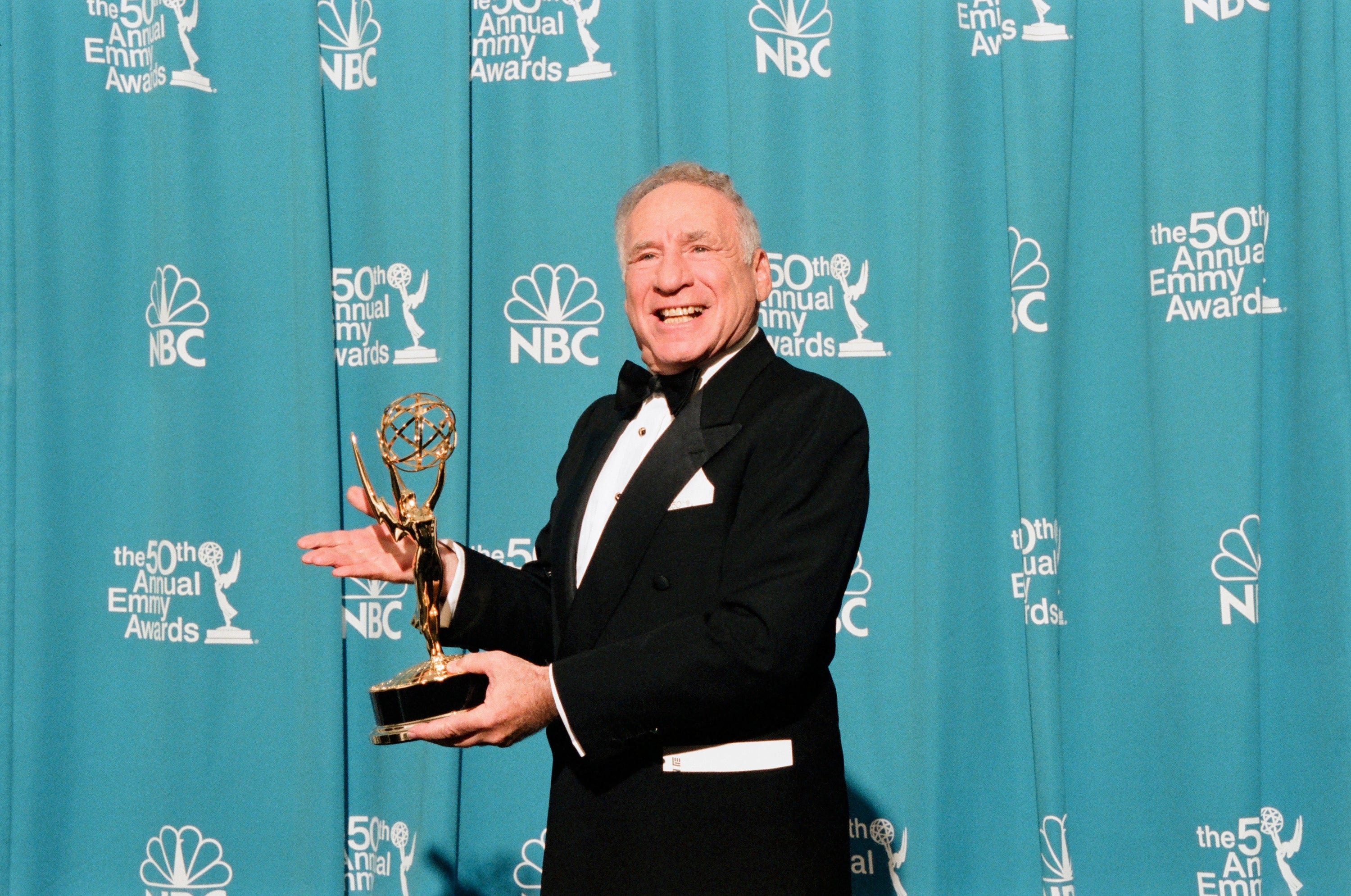 Person in tuxedo holding Emmy award, smiling at 50th Annual Emmy Awards backdrop
