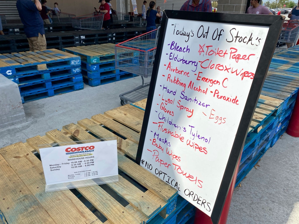 Sign lists items out of stock at a store, including toilet paper, sanitizer, and wipes. A Costco notice mentions item limits and unavailable optical orders
