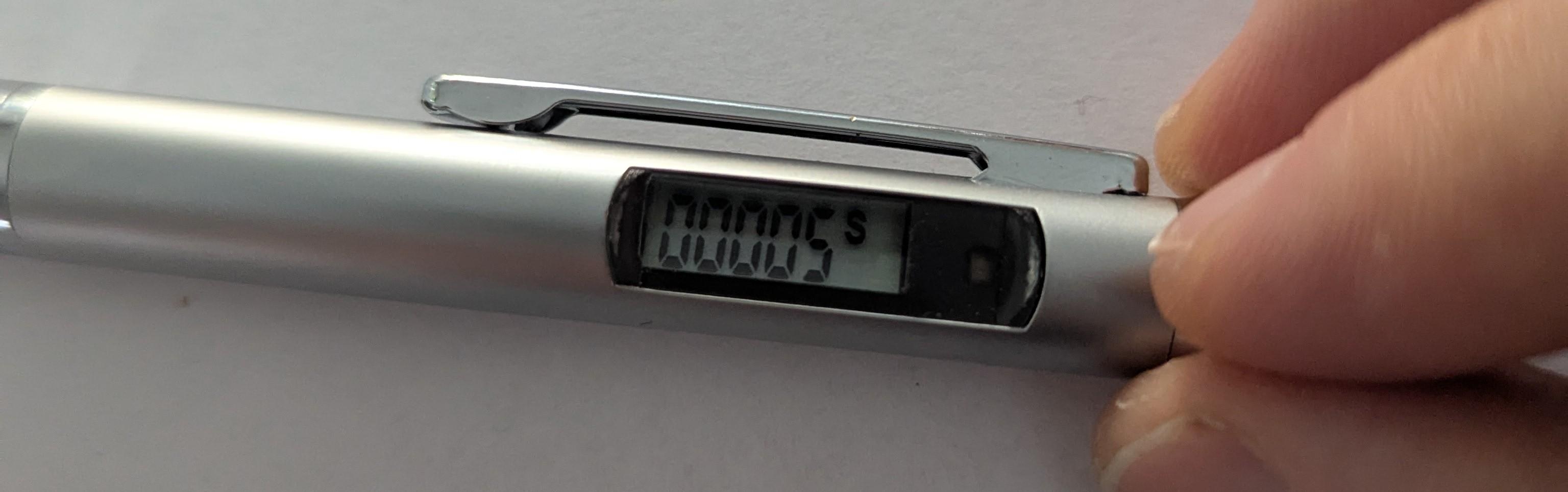 Electronic pen with a display showing "00005" followed by a numerical code. A hand is holding the pen