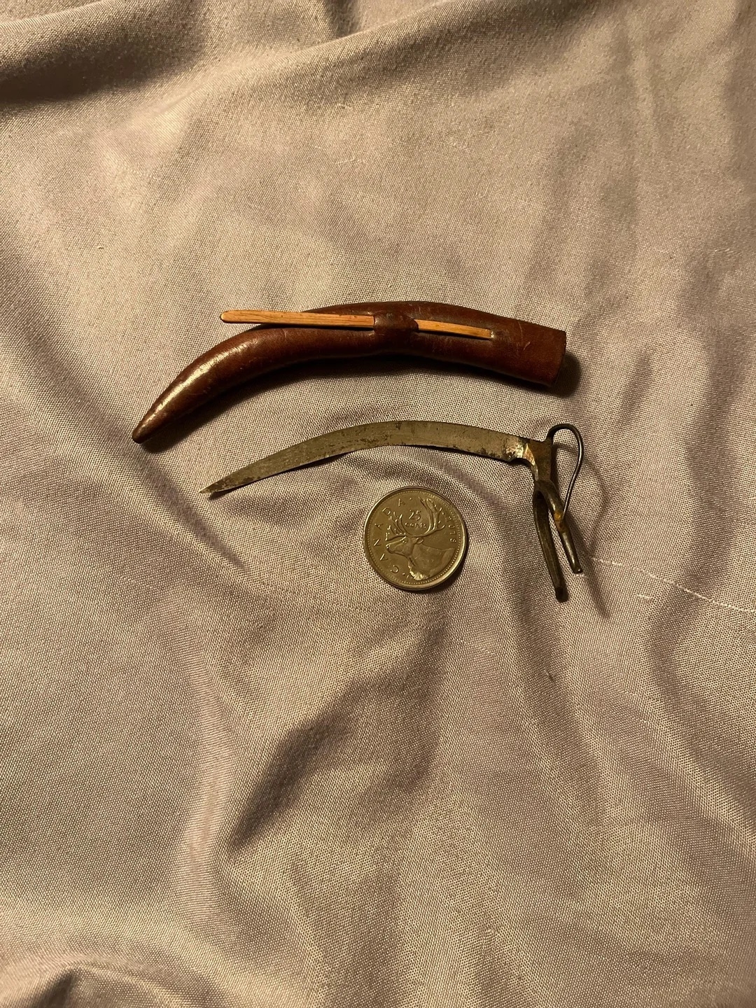 Two rustic metal tool, leather sheath and a coin are placed on fabric, showcasing their size and shape for comparison