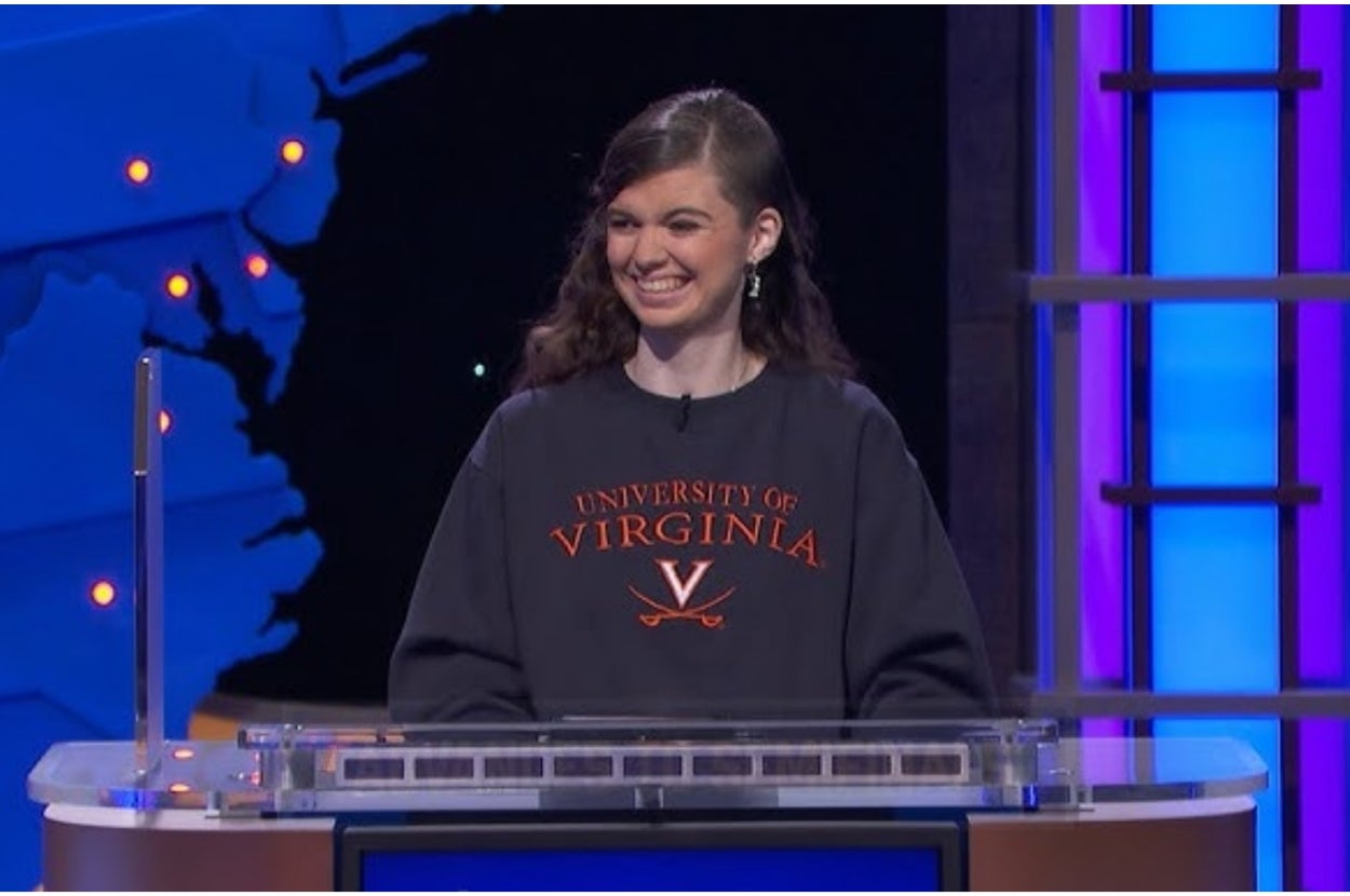 Person on a TV game show stage wearing a University of Virginia sweatshirt, smiling at a podium