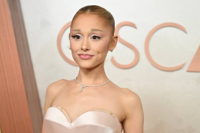 Person in strapless gown with sleek, styled hair and elegant necklace at a formal event background