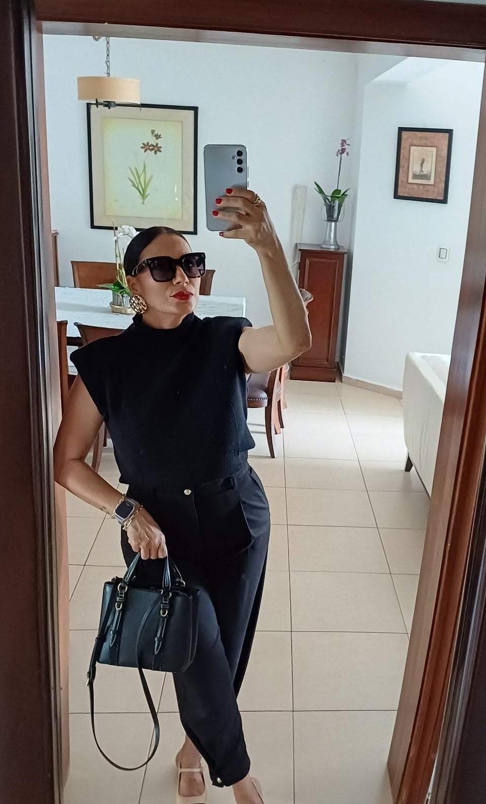Orang mengambil mirror selfie dengan pakaian hitam bergaya, memegang tas tangan, di dalam ruangan