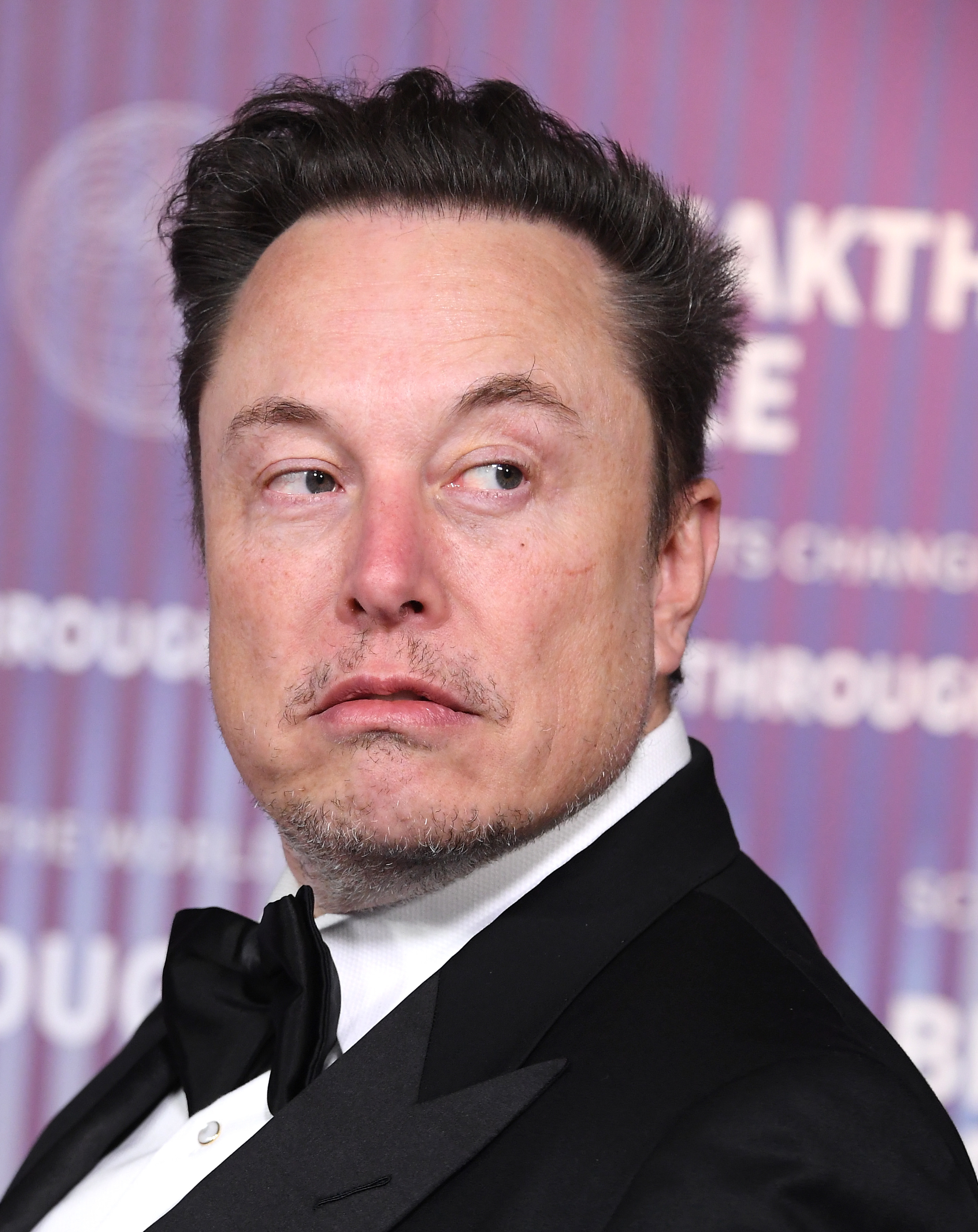 Elon Musk in a tuxedo with a bow tie, looking to the side, at a formal event or red carpet