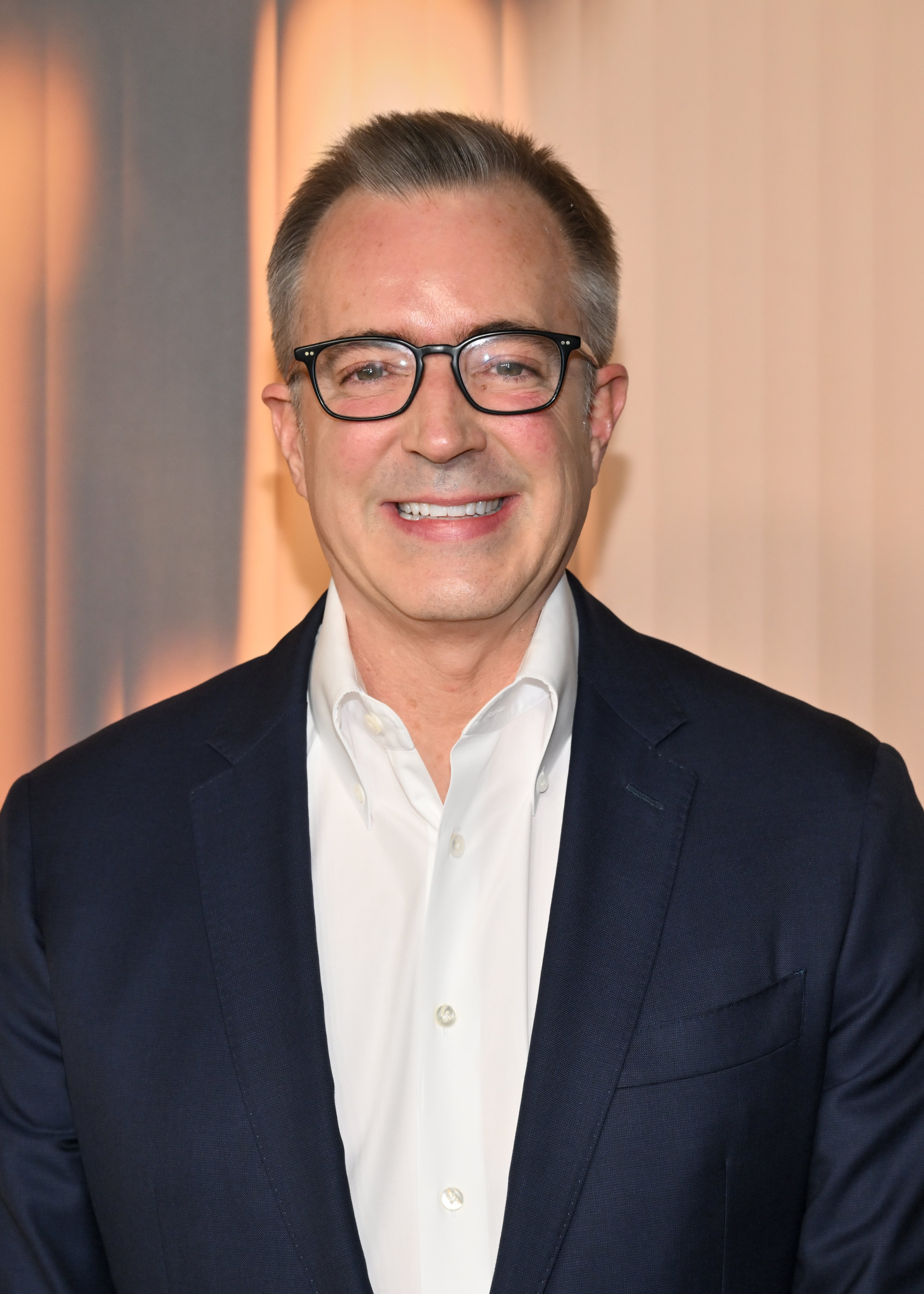 Person in glasses and suit jacket over button-up shirt, smiling at the camera