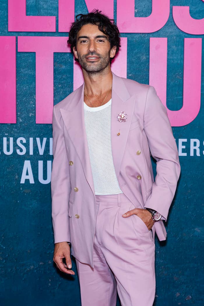 Man on red carpet in a stylish double-breasted suit with a mesh shirt and wristwatch, posing confidently