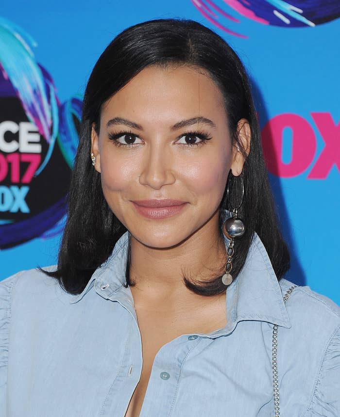Naya Rivera in denim shirt with large earrings, attending a 2017 event with colorful background