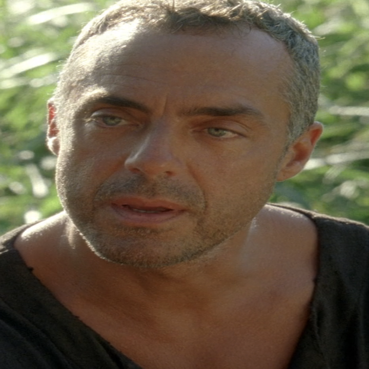 Titus as the man in black in lost with short hair, wearing a casual dark T-shirt, is outdoors amidst greenery, appearing thoughtful