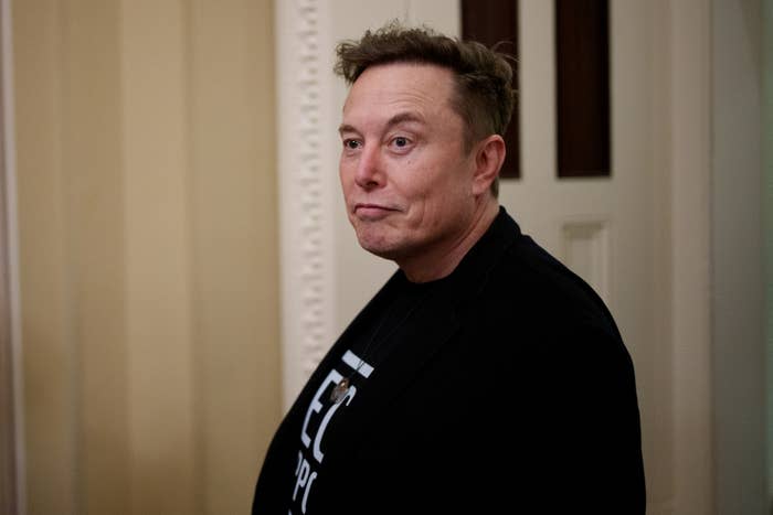 Person in a blazer and graphic tee stands indoors, facing slightly left