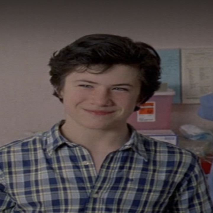 Dylan as David in Lost smiling, wearing a plaid shirt, standing in a room with medical posters in the background