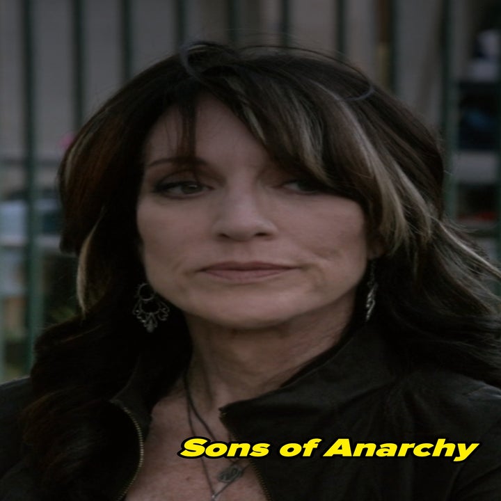 Katey Sagal in Sons of Anarchy with long hair wearing a jacket, with a neutral expression, standing outdoors
