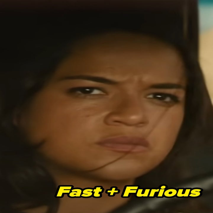 Letty in fast and furious looking serious while sitting in a car, hands on the steering wheel, gazing forward with a concentrated expression