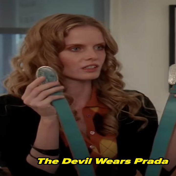 Rebecca Mader in Devils Wears Prada with long hair holds a turquoise belt, wearing a patterned top and black cardigan, standing indoors