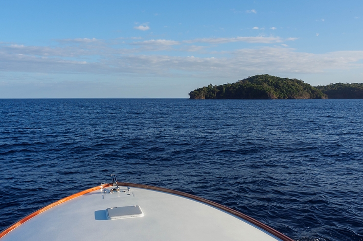 ボートの船首から見た広い海と遠くの小さな島。青空が広がる風景。