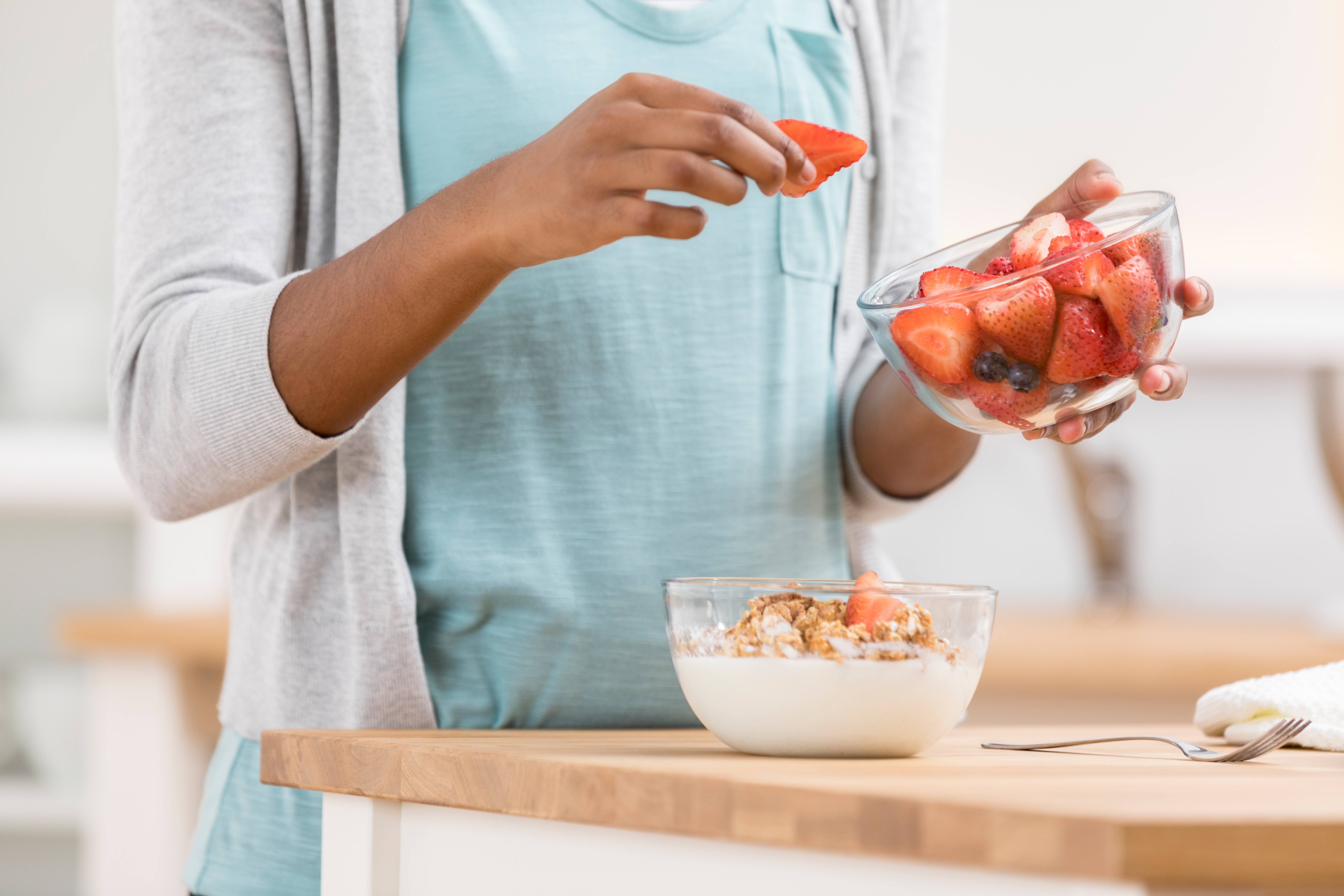 Person som legger friske jordbær i en skål med yoghurt toppet med granola på en kjøkkenbenk