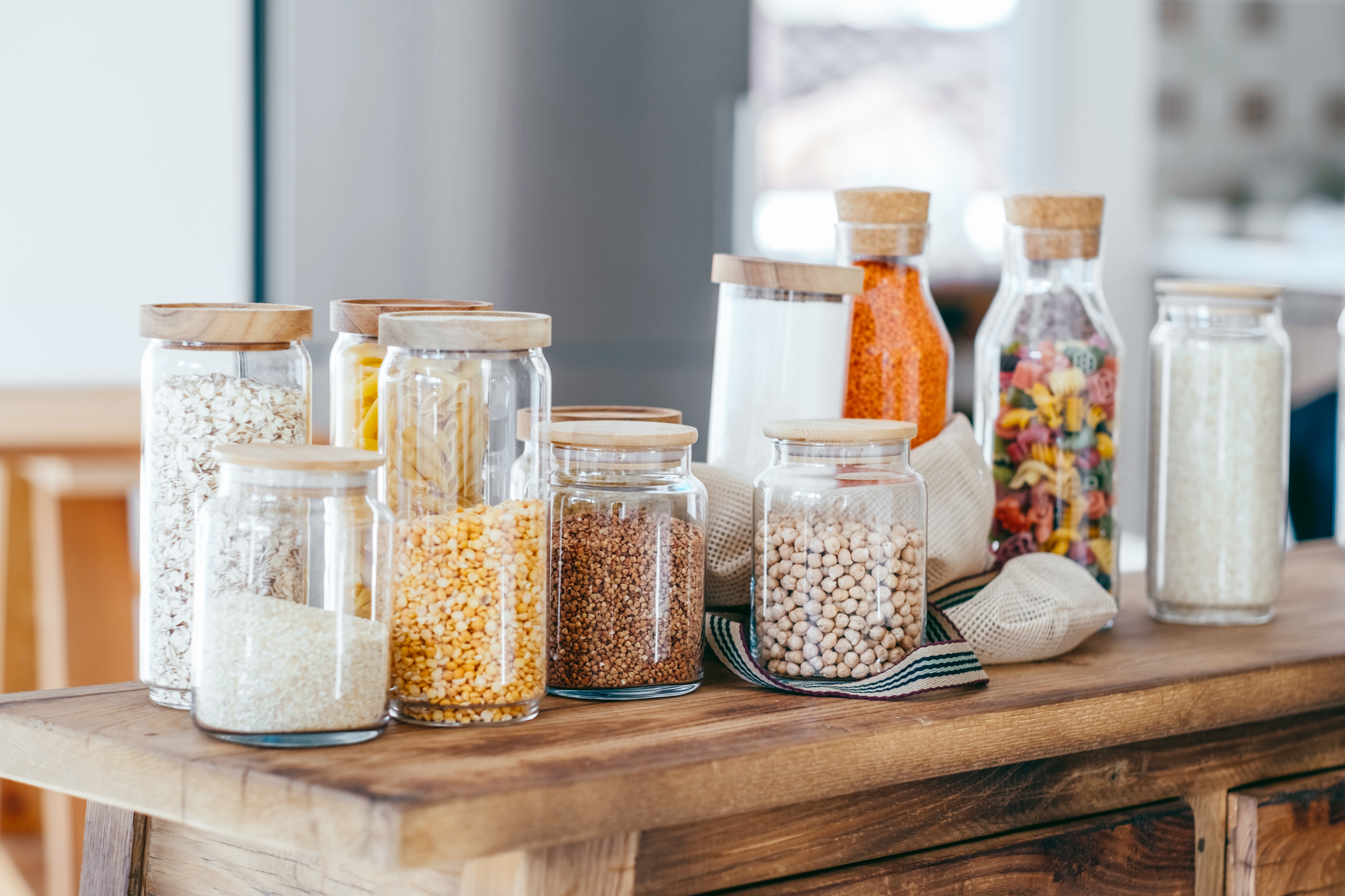 Various glass jars filled with grains, pasta, and spices are arranged on a wooden table