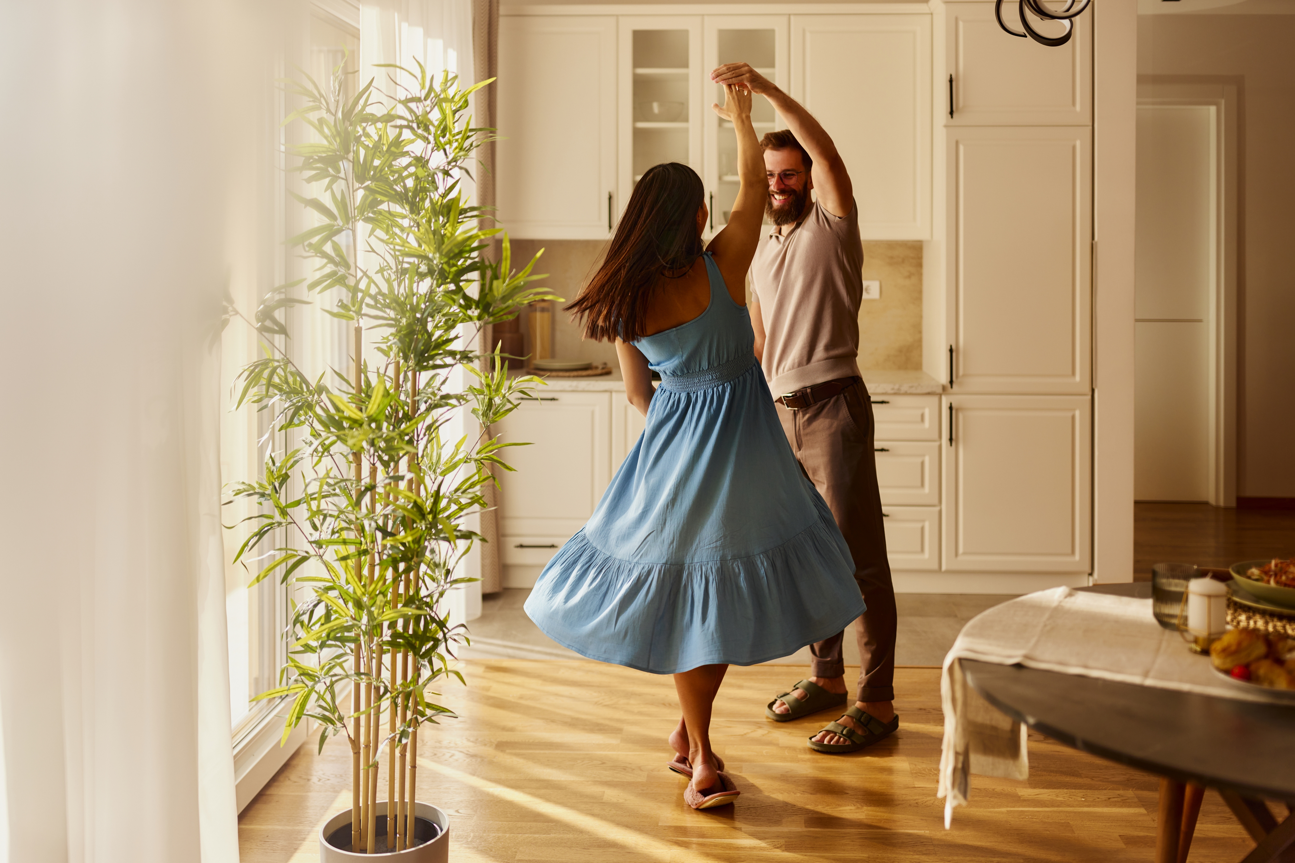Et par danser med gledelig på et solfylt kjøkken, kvinnen i en flytende kjole, omgitt av koselig innredning av hjemmet