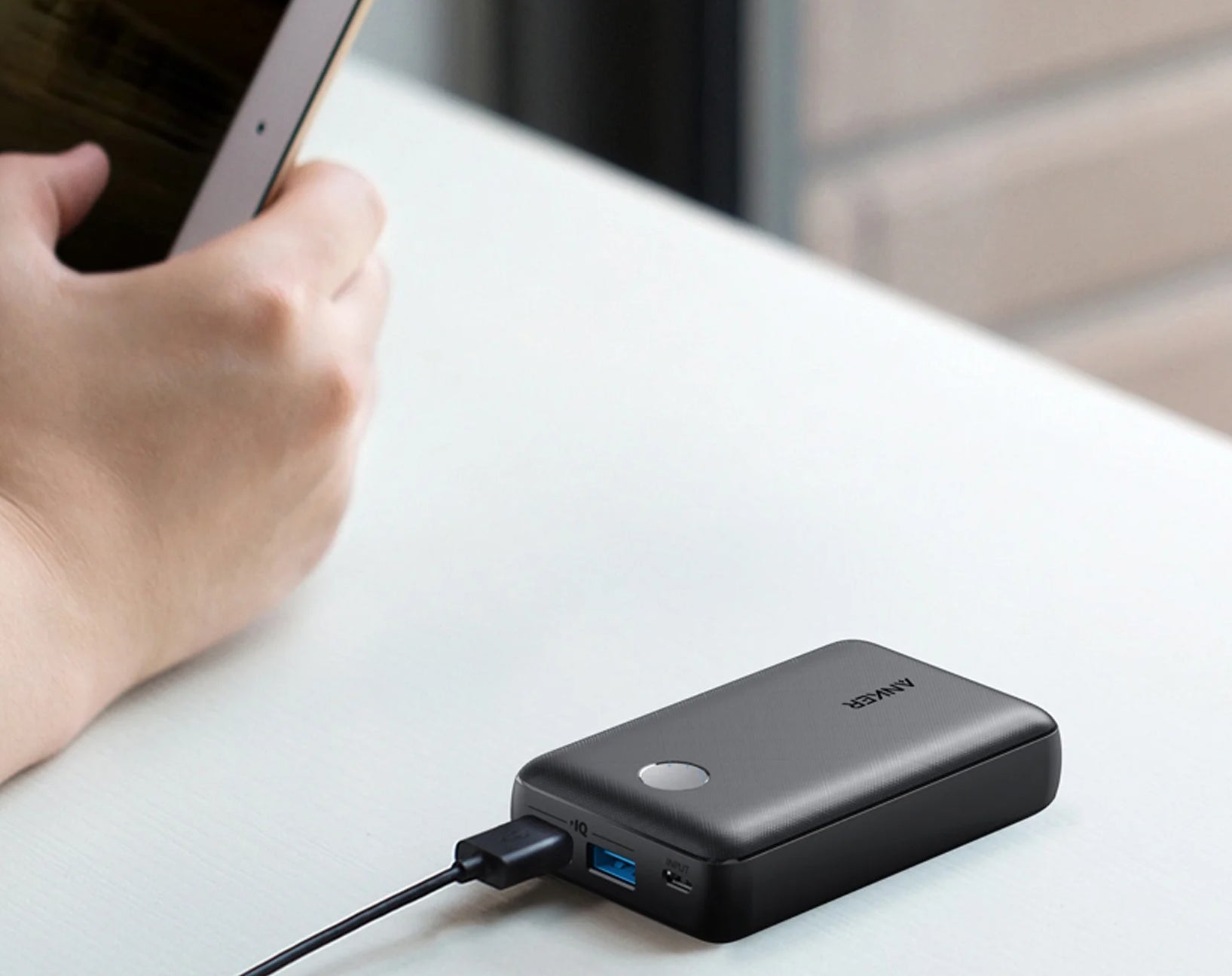 Person using a tablet connected to a compact external power bank on a desk
