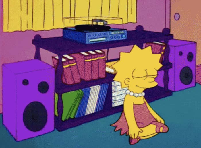 Animated character Lisa Simpson meditates in front of a speaker, enjoying music. She sits cross-legged, eyes closed, in a peaceful environment