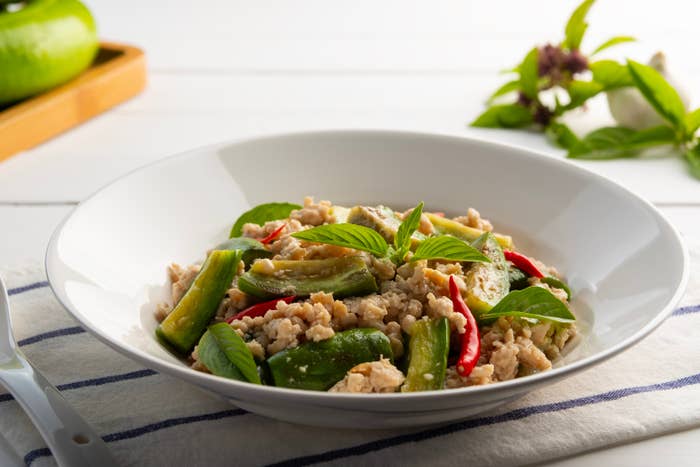A bowl of stir-fried chicken and vegetables, garnished with fresh basil leaves, on a white tablecloth