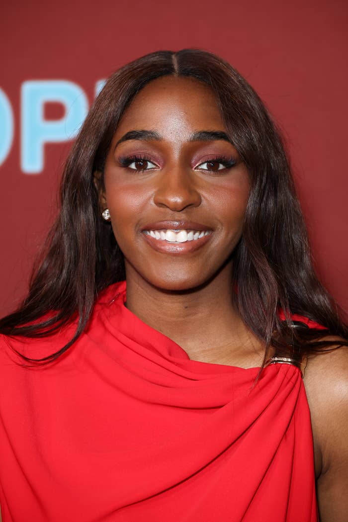 Ayo Edebiri in elegant red draped gown on a red carpet, smiling at the event