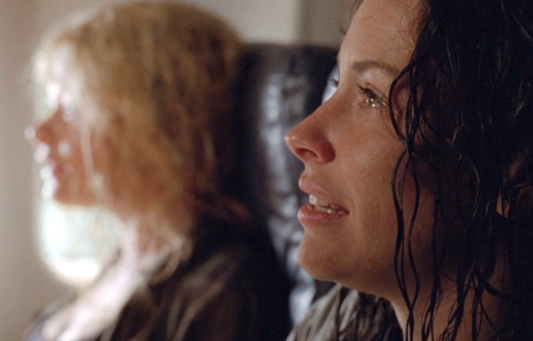 Kate and Claire sitting on a plane. Kate, with wet hair, looks emotional; Claire is in the background, slightly blurred