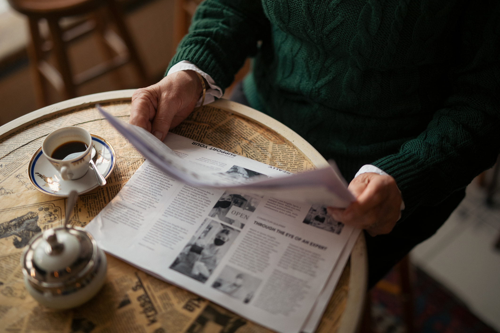 Person reads newspaper with a cup of coffee on a wooden table