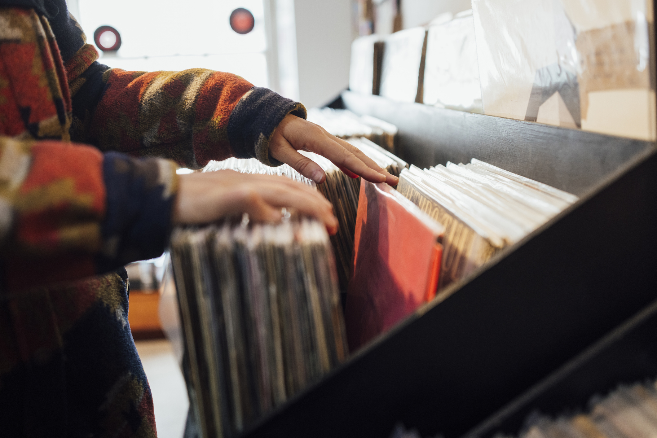 Person browsing through vinyl records in a record store, showcasing a retro or nostalgia theme