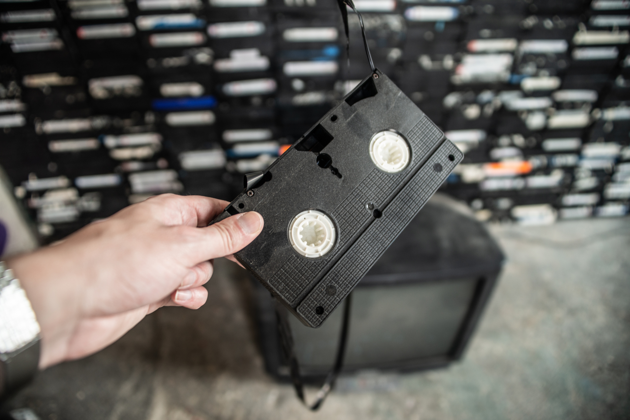 Hand holding a VHS tape in front of a stack of tapes, symbolizing nostalgia and retro technology