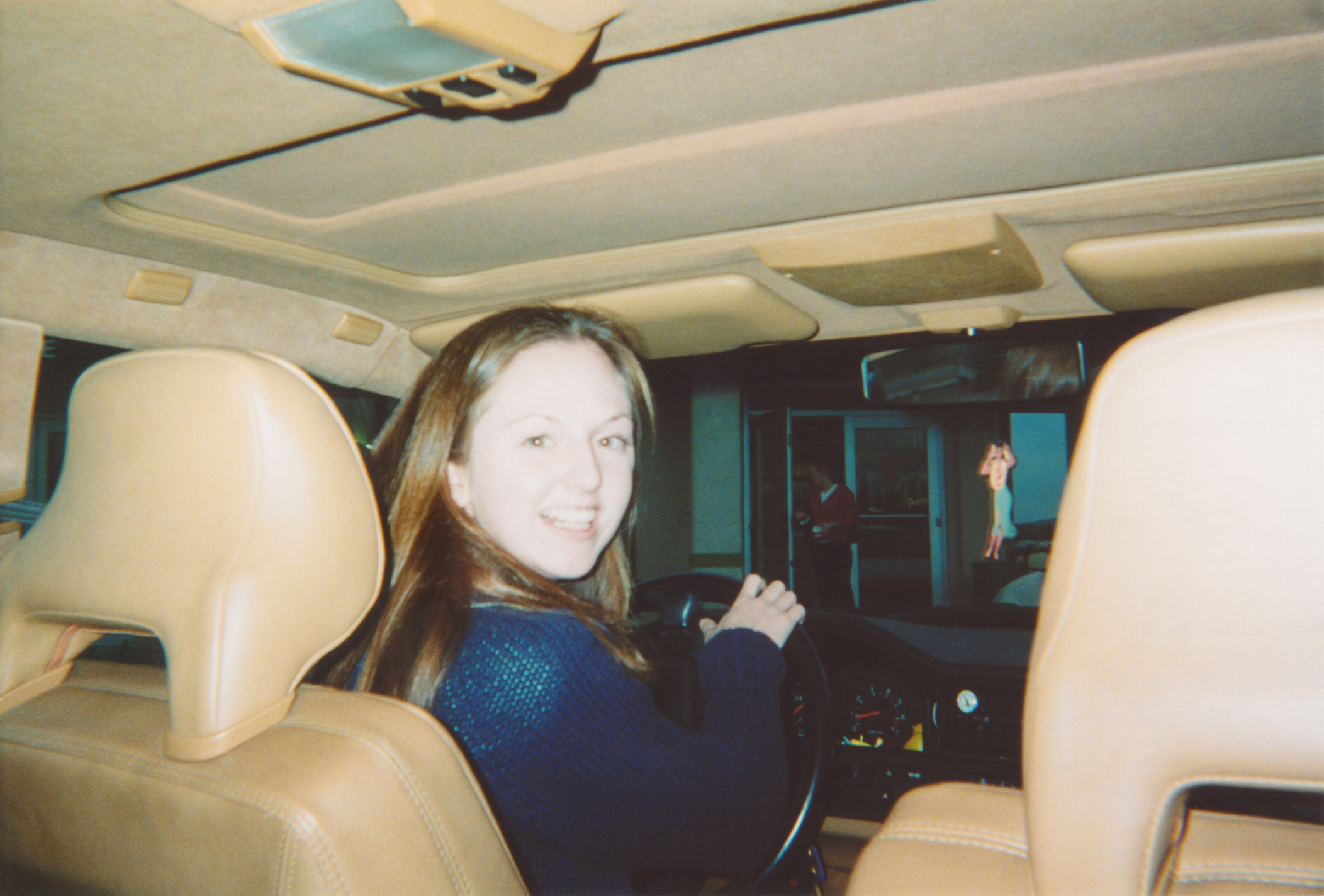 Woman sitting in the driver&#x27;s seat of a car, looking back and smiling at the camera