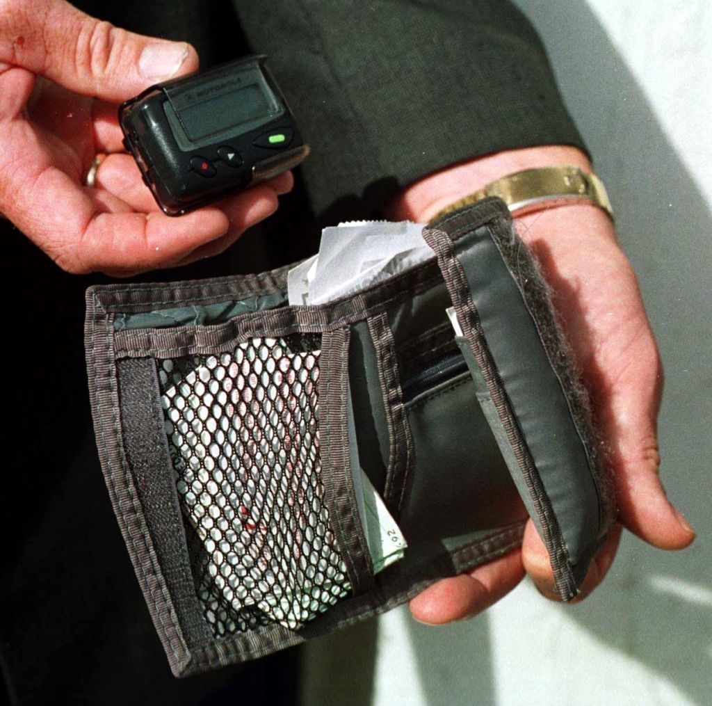 Person holding a pager and open wallet with compartments, including a netted section holding small items, possibly from the 1990s
