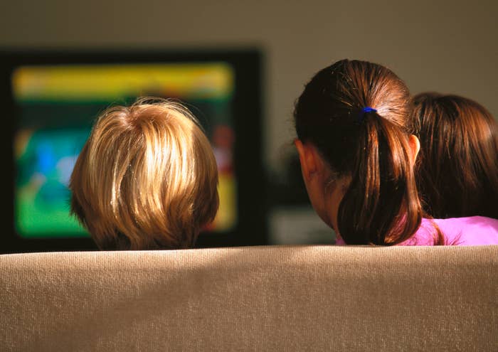 Three people watching TV from a couch, seen from behind, focusing on the screen