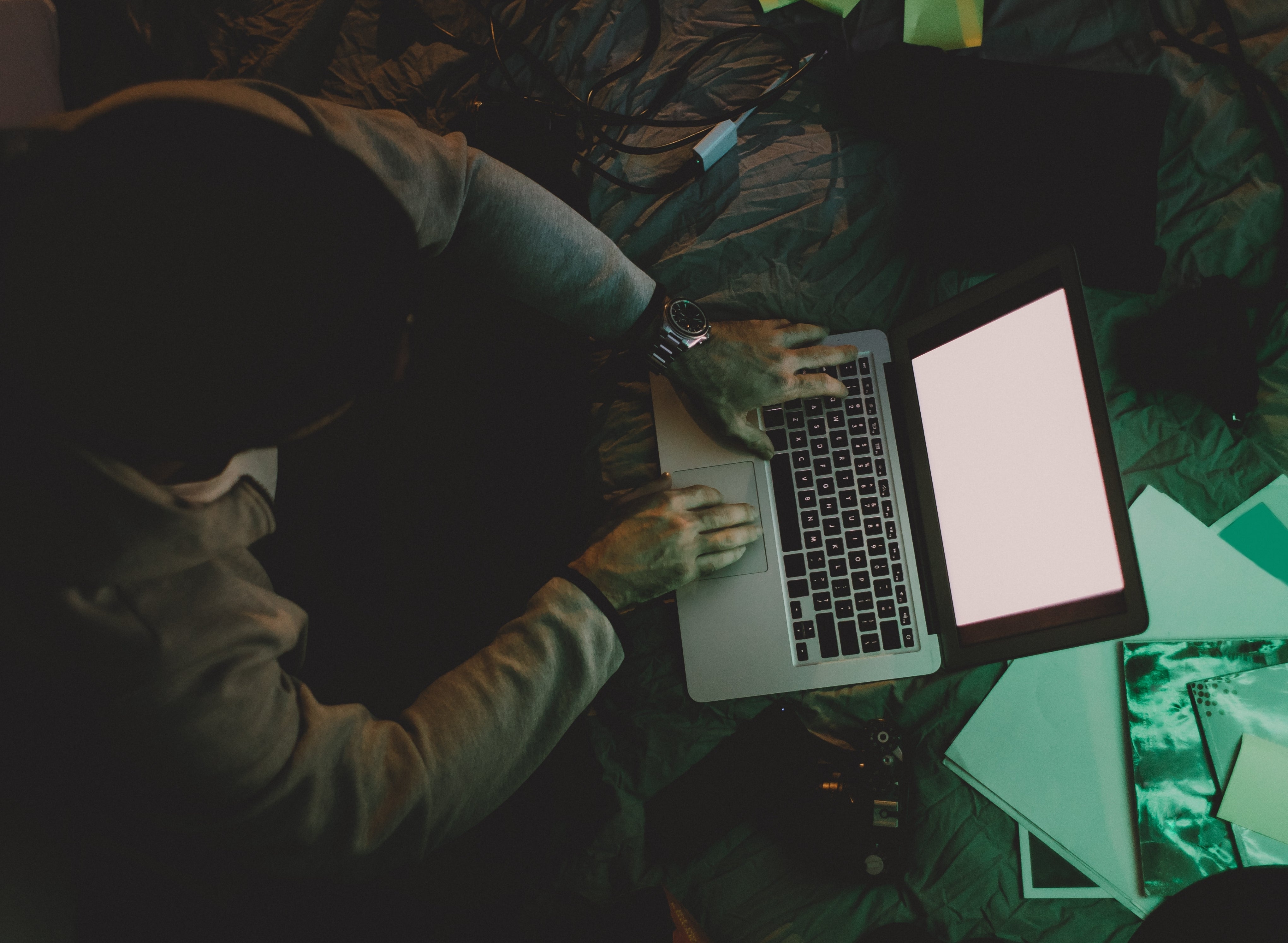 Person using a laptop on a cluttered floor with cables and papers around