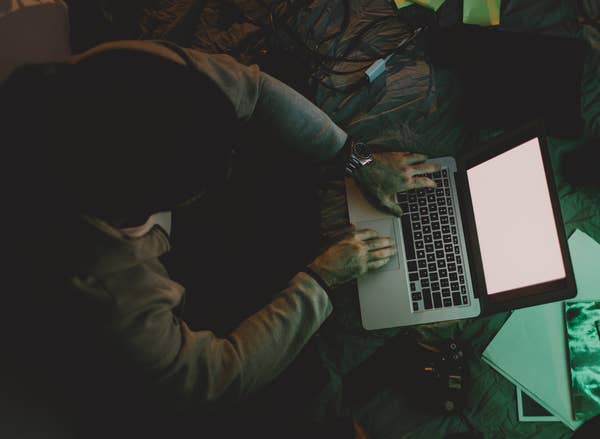Person using a laptop on a cluttered floor with cables and papers around
