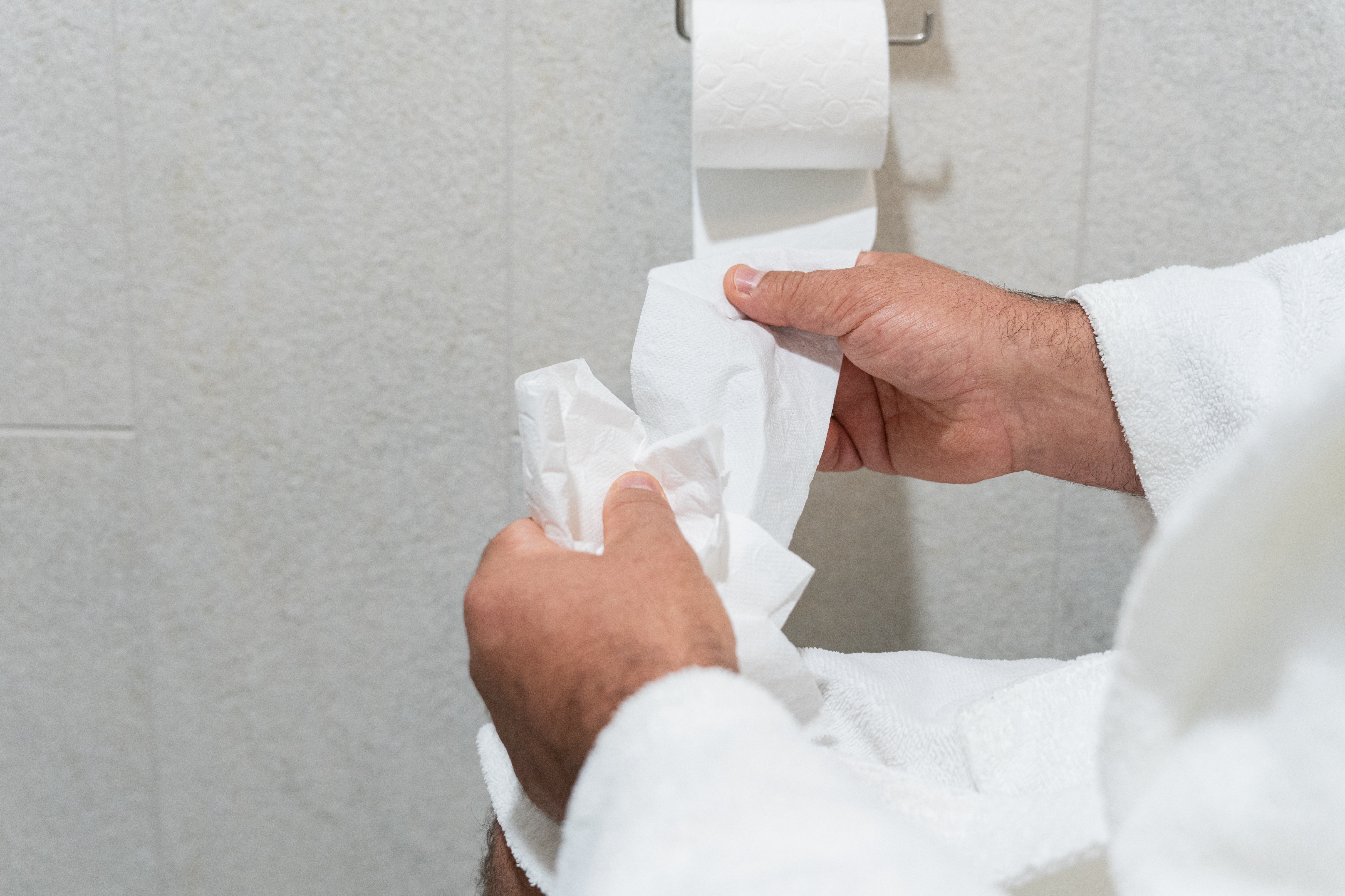 Person in a bathrobe handling toilet paper in a bathroom setting