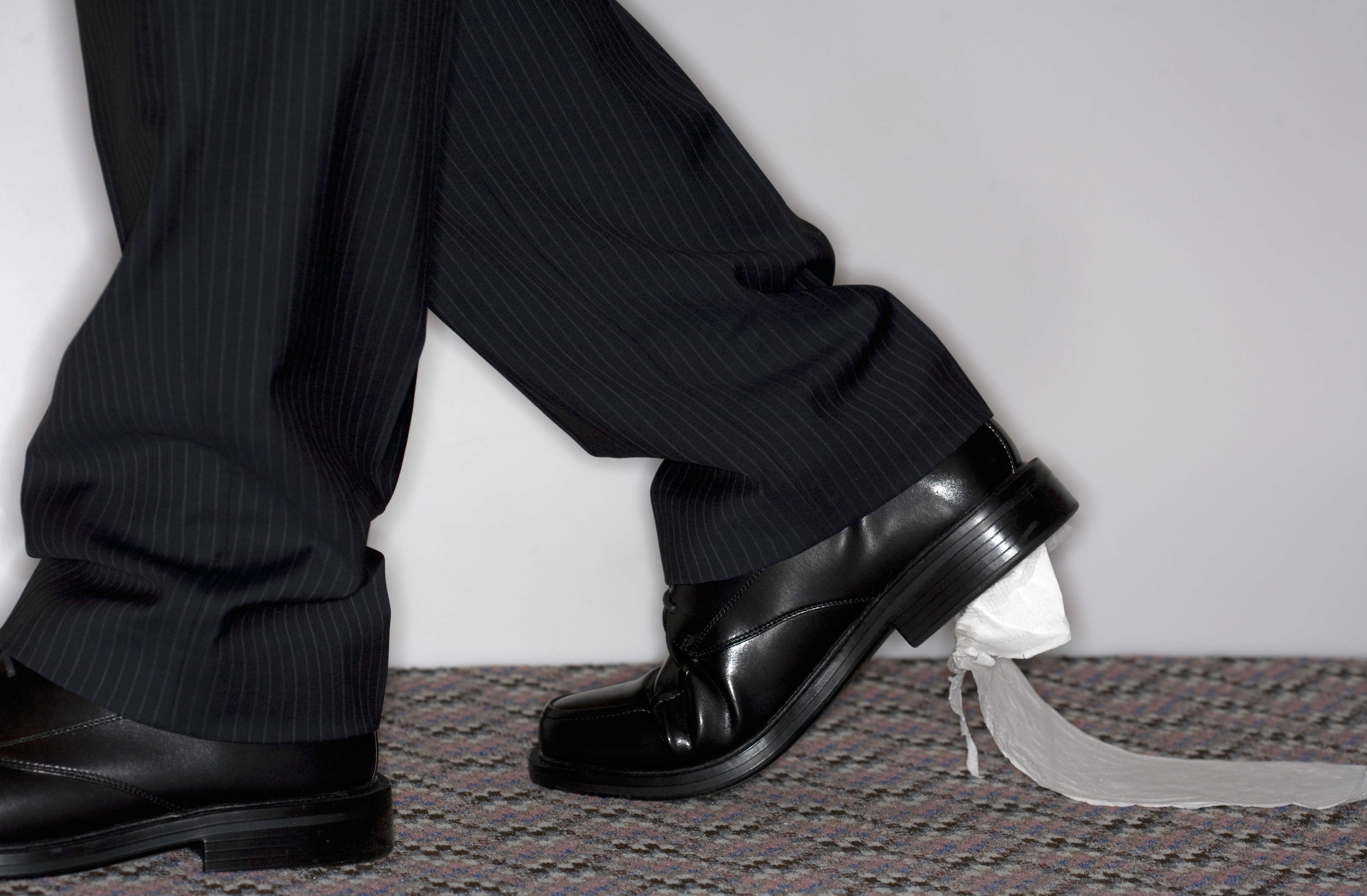 Person in suit accidentally dragging toilet paper stuck to shoe