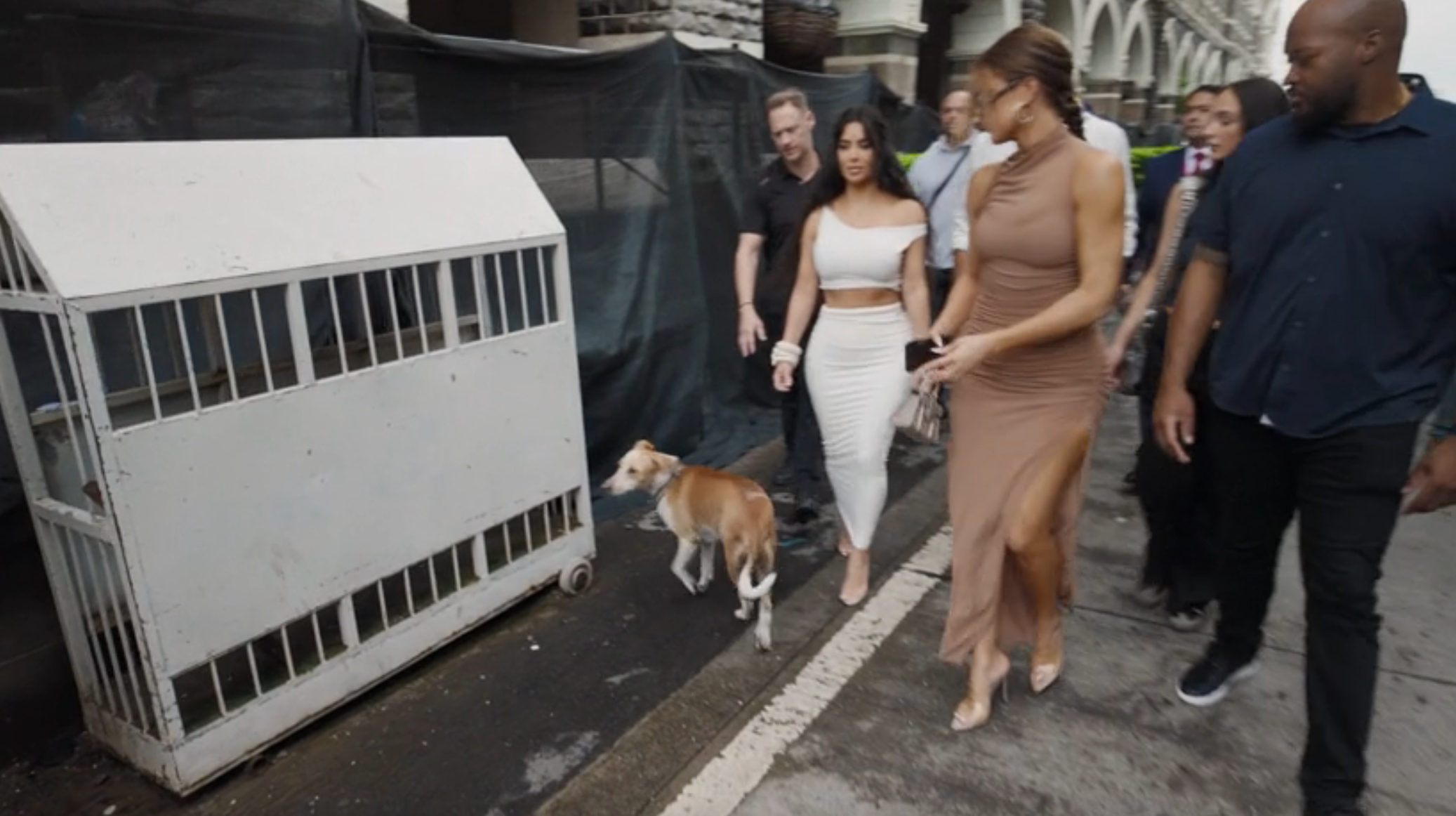 A stray dog approaches Kim and Khloe as they walk through Mumbai with a crowd of people