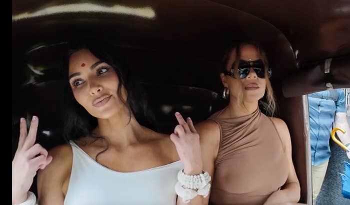 Kim and Khloe sit in a rickshaw in stylish sleeveless outfits, posing with peace signs; Kim wears a bindi and Khloe sunglasses