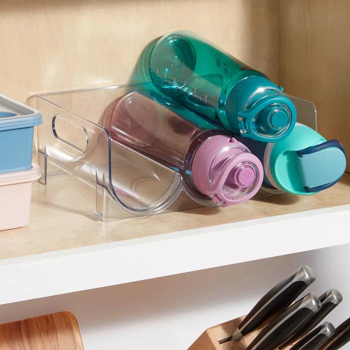 Water bottles stored successful a wide organizer connected a shelf, alongside integrative nutrient containers, suggesting a tidy room retention solution